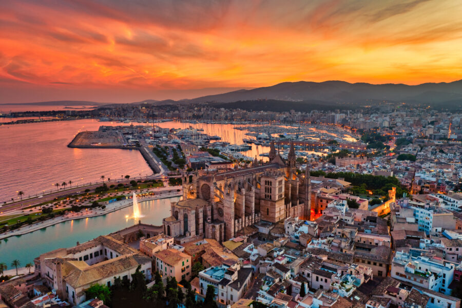 Sunset aerial view of the Cathedral of Santa Maria of Palma, highlighting its intricate Gothic design and surrounding landscape