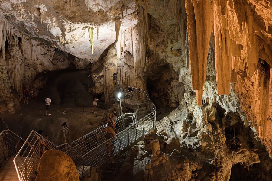 People descend a staircase inside the Cave of Antiparos in Greece, surrounded by stunning rock formations.