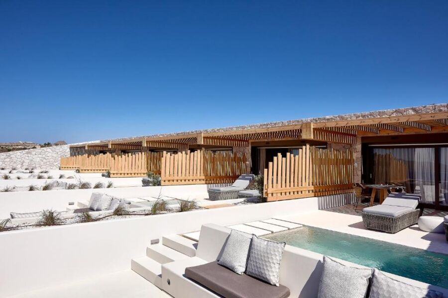 Scenic pool area at Cave Suites Milos, a beach resort in Greece, surrounded by sun loungers and palm trees.