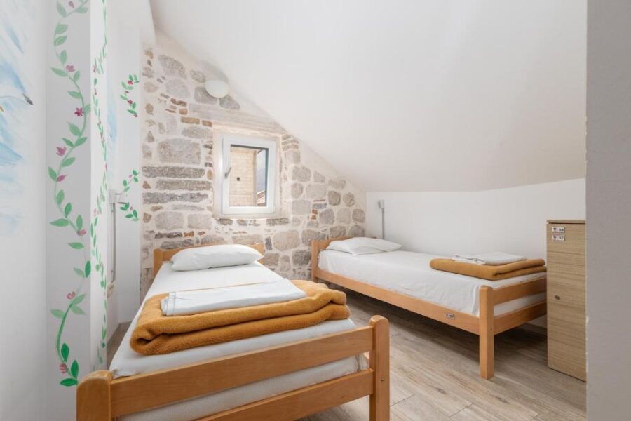 Two beds in a small room with a stone wall, located in CENTRUM HOSTEL, Kotor Old Town.
