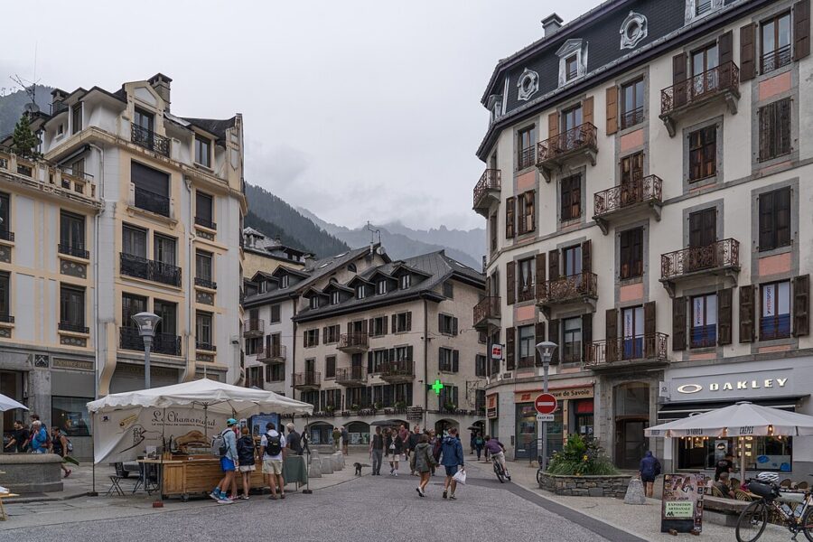 People stroll and gather on a vibrant Chamonix-Mont-Blanc street, creating a lively scene of community and activity.
