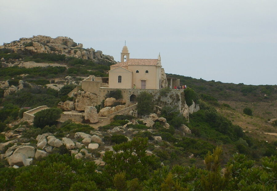 Chapel of Notre Dame de la Serra perched on a rocky hillside, featuring a prominent tower against a clear blue sky.