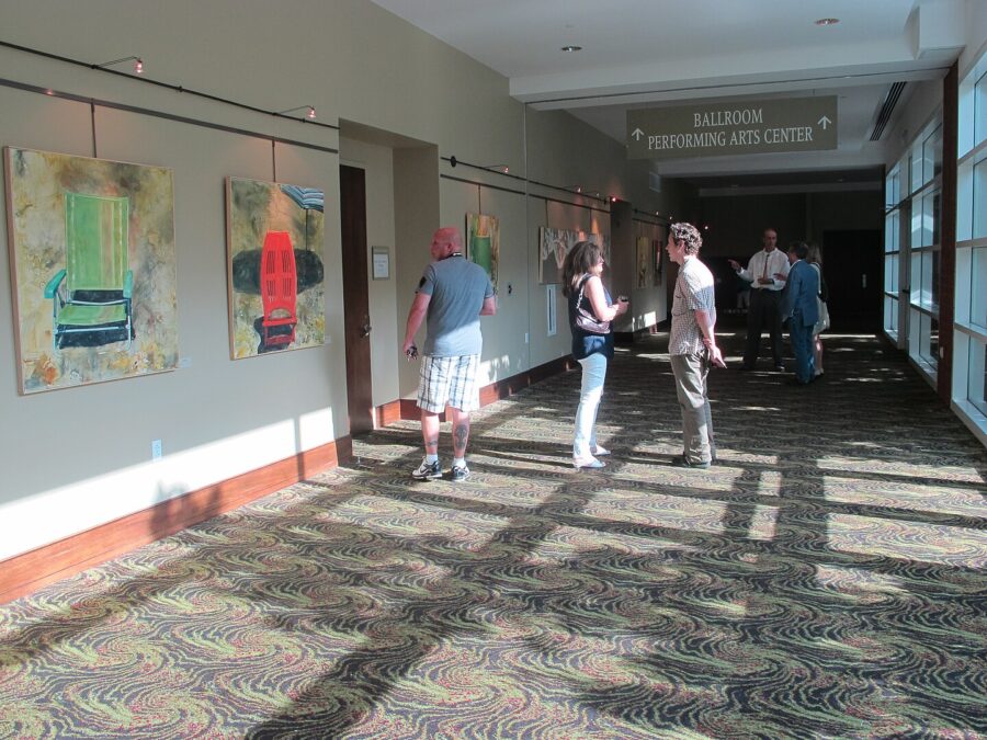 Attendees stroll down a hallway featuring various paintings at the Charleston Area Convention Center.
