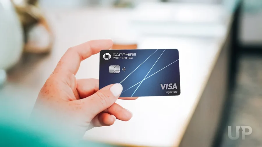 Chase Sapphire Preferred credit card in hand, sleek blue design with Visa logo, kitchen background.