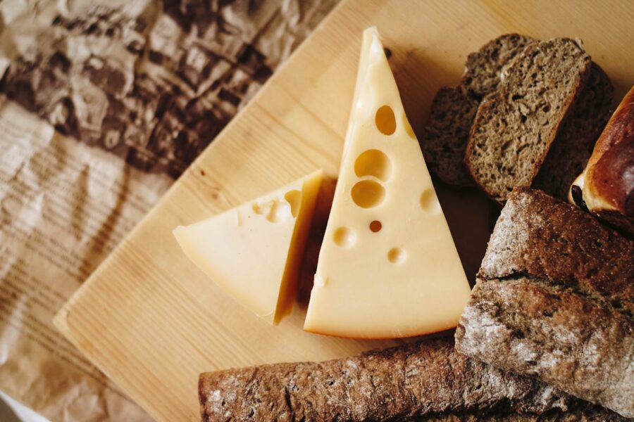 Rustic platter with Swiss cheese wedges, whole-grain bread, and glazed roll on wooden board.