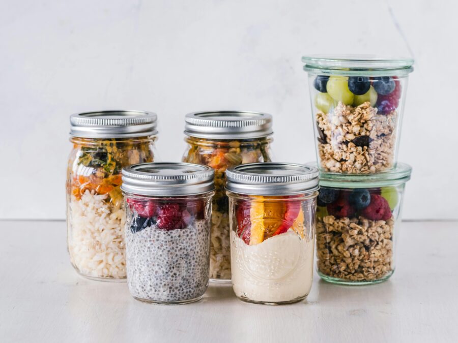 Colorful mason jars filled with healthy meals: yogurt, chia pudding, granola, fruits, and grains.