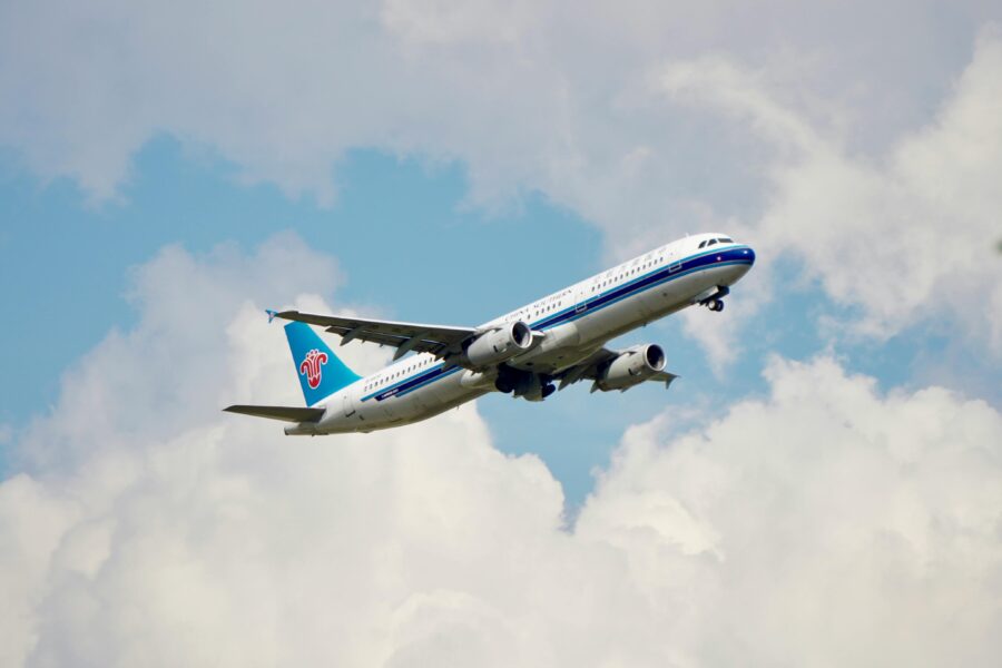 Modern commercial airplane performing aerial maneuver against a dynamic sky with clouds.