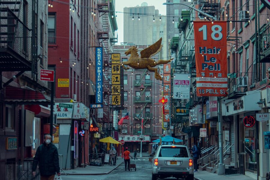 Chinatown street scene with vibrant storefronts, golden winged figure, and bustling pedestrian activity.