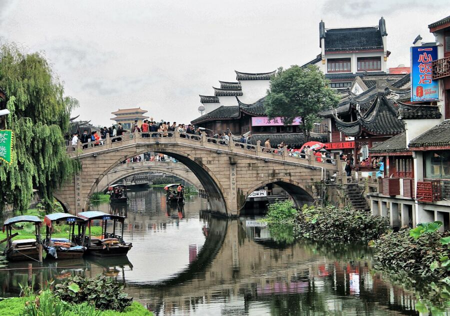 Traditional Minhang with stone bridge, canal, wooden buildings, and lush greenery.