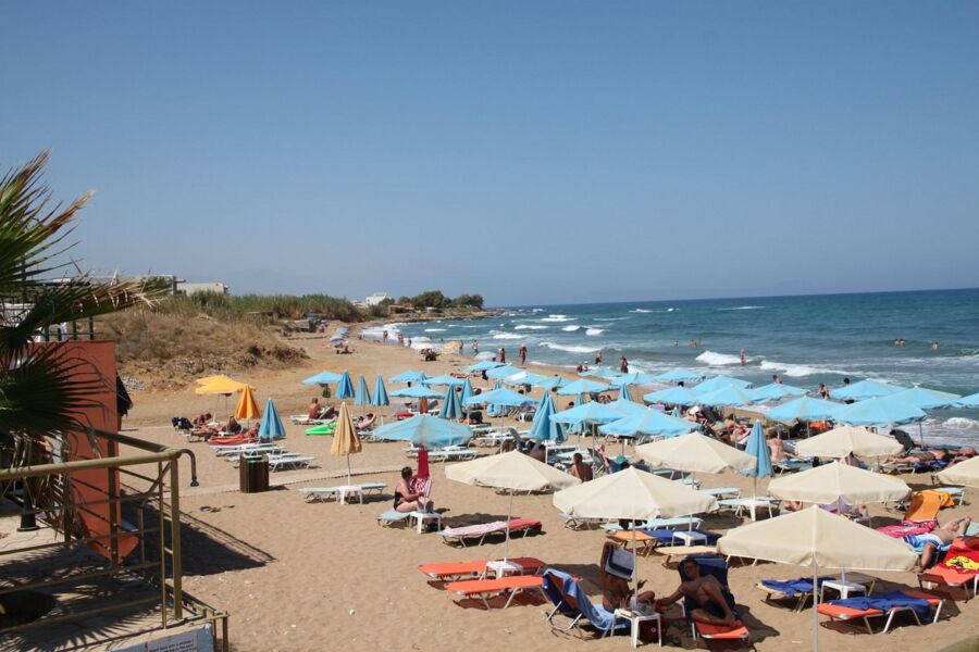 Crowded Chrissi Akti beach in Greece, featuring sunbathers and vibrant umbrellas dotting the sandy shore.