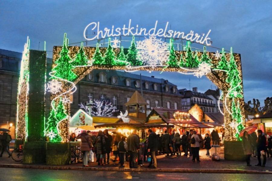 Christmas market arch lights over festive wooden stalls and evening crowd.