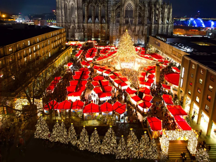 Christmas market at night before Gothic cathedral, festive lights and crowded stalls.