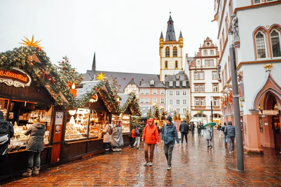 Germany Christmas market in old town on wet cobblestones with festive stalls and church tower.