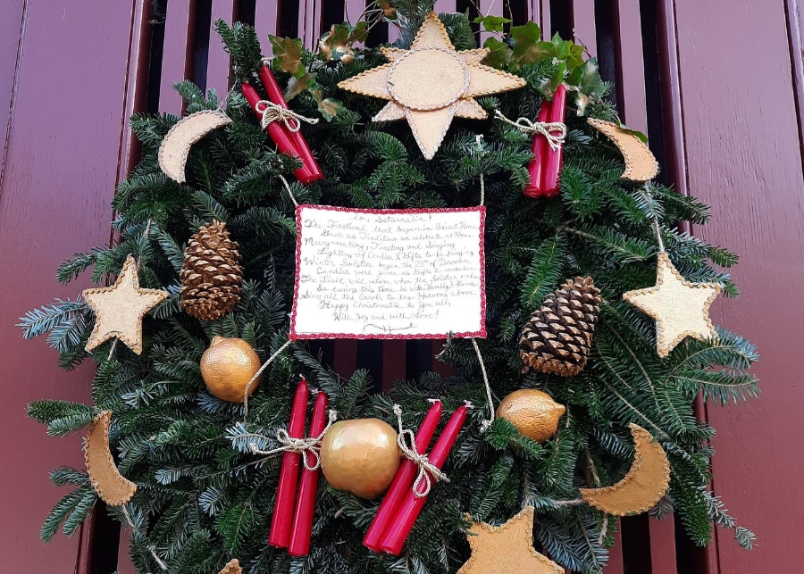Festive wreath with candles and a poem displayed on a door, part of the Christmastide in Virginia exhibit.