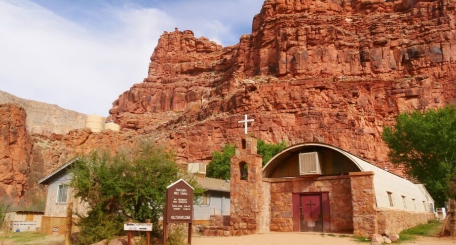 Red cliffs, church with bell tower, and modern building in desert landscape.