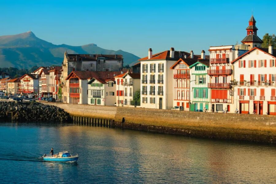 Colorful boat glides through the water, with bright buildings of Ciboure, French Basque Country in the background.
