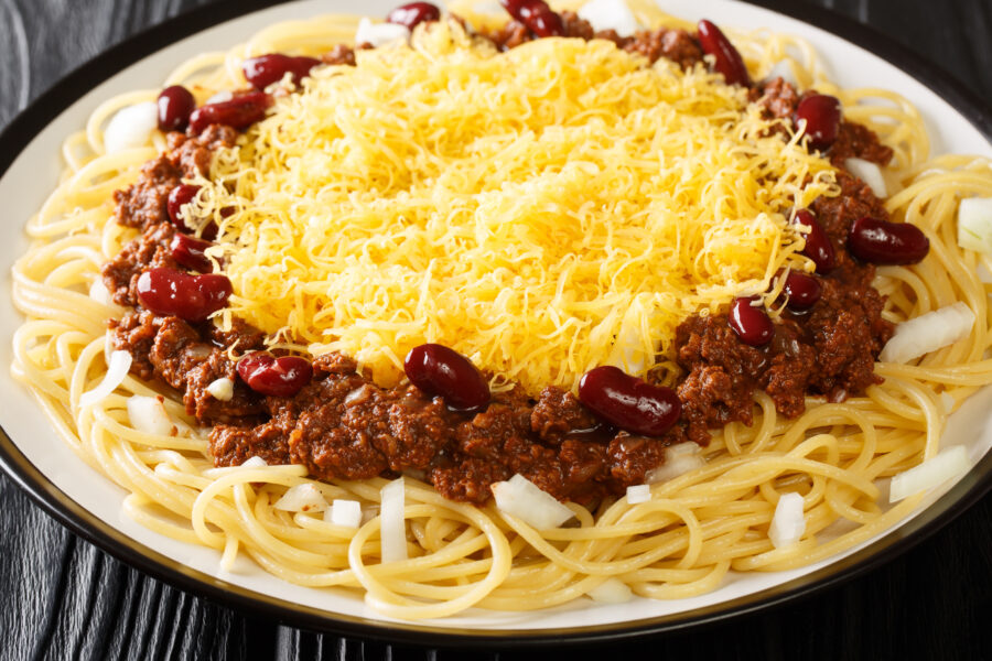 Plate of Cincinnati style chili 5-way, captured in close-up on a textured black wooden surface