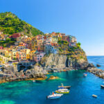 Manarola traditional typical Italian village in National park Cinque Terre, colorful multicolored buildings houses on rock cliff, fishing boats on water, blue sky background, La Spezia, Liguria, Italy