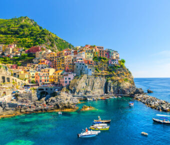 Manarola traditional typical Italian village in National park Cinque Terre, colorful multicolored buildings houses on rock cliff, fishing boats on water, blue sky background, La Spezia, Liguria, Italy