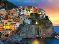 Sunset over Cinque Terre coastal village with colorful buildings and sea view.
