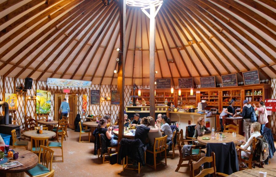 Circular yurt restaurant interior with rustic wooden decor, vibrant artwork, and cozy dining ambiance.