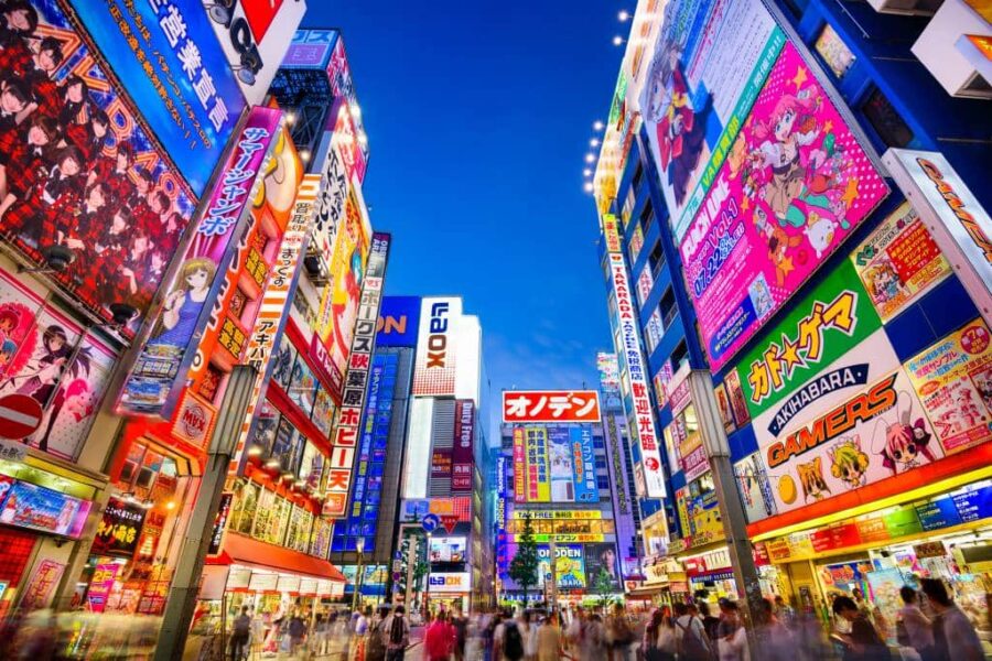 Akihabara Tokyo street with neon anime billboards, electronics shops, and crowded evening pedestrians.