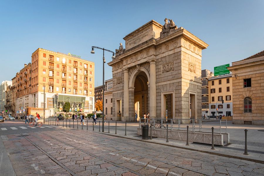 Historic stone archway in vibrant urban setting featuring modern and traditional architecture at sunset.
