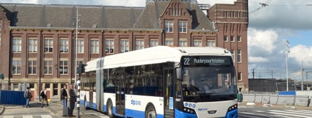 GVB articulated city bus route 22 to Muiderpoortstation turning at Amsterdam intersection with historic building.