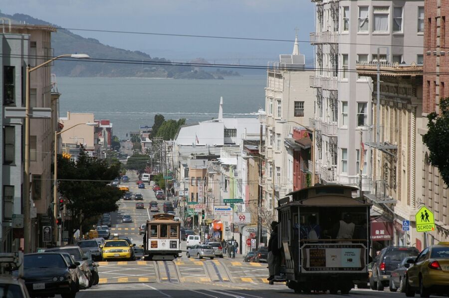 San Francisco street scene with cable car, steep hill, diverse architecture, and bay view.