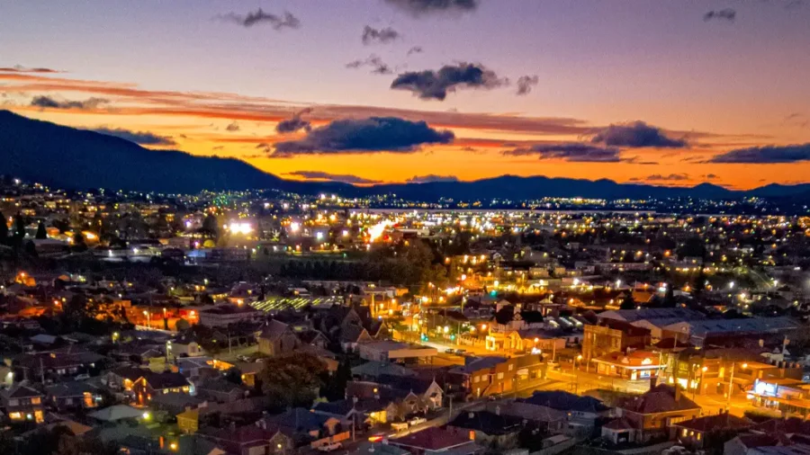 North Hobart city lights at dusk with glowing skyline, mountains, sunset, and vibrant nightlife.