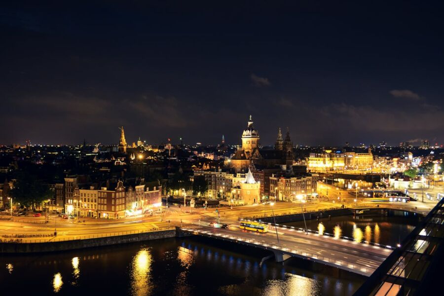 Amsterdam night skyline with bridge, illuminated architecture, water reflections, and historical tower.