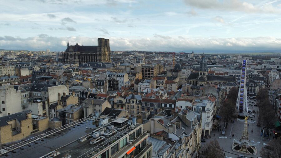 Reims, France panoramic rooftops with Gothic cathedral and Ferris wheel under overcast sky.