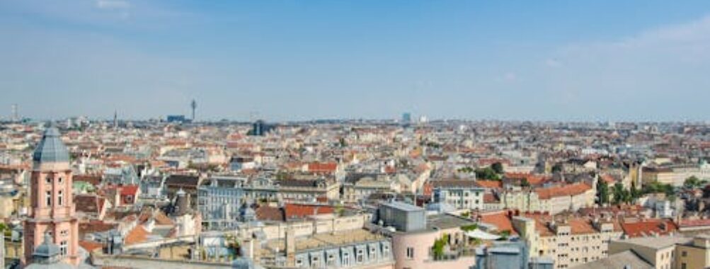 Sunlit panoramic aerial view of historic city rooftops with red tile roofs and skyline.