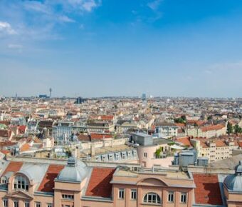 Sunlit panoramic aerial view of historic city rooftops with red tile roofs and skyline.
