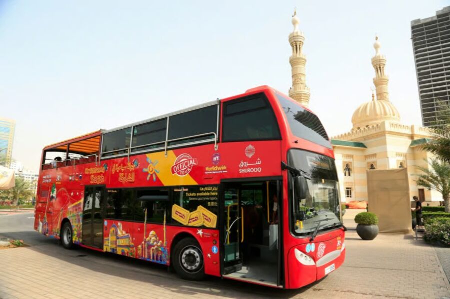 Red double-decker bus stands in front of a mosque, showcasing the City Sightseeing Hop-On Hop-Off Tour in Sharjah.