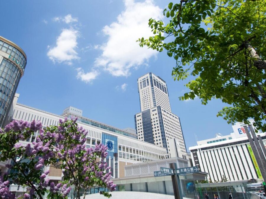 JR Tower Sapporo city skyline with modern station building, skyscrapers and blooming lilac flowers.
