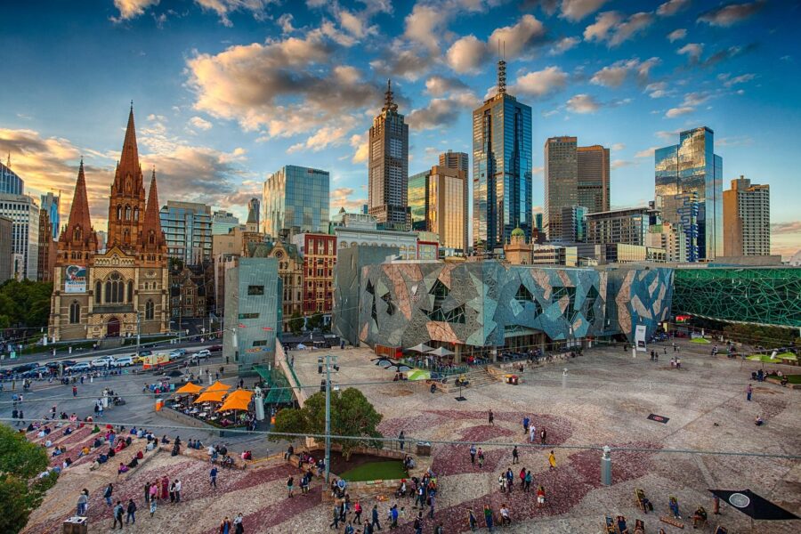 Federation Square city plaza with cathedral, modern museum buildings and skyscrapers at sunset.