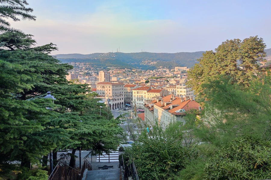 Trieste city overlook from stairway with terracotta roofs and rolling hills in Italy.