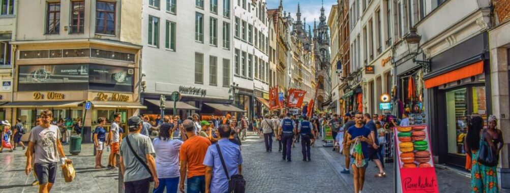 Bustling European city street with historic and modern architecture, shops, and lively crowd.