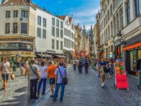 Bustling European city street with historic and modern architecture, shops, and lively crowd.