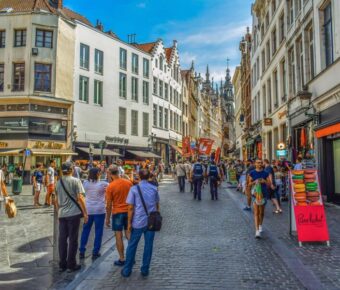 Bustling European city street with historic and modern architecture, shops, and lively crowd.