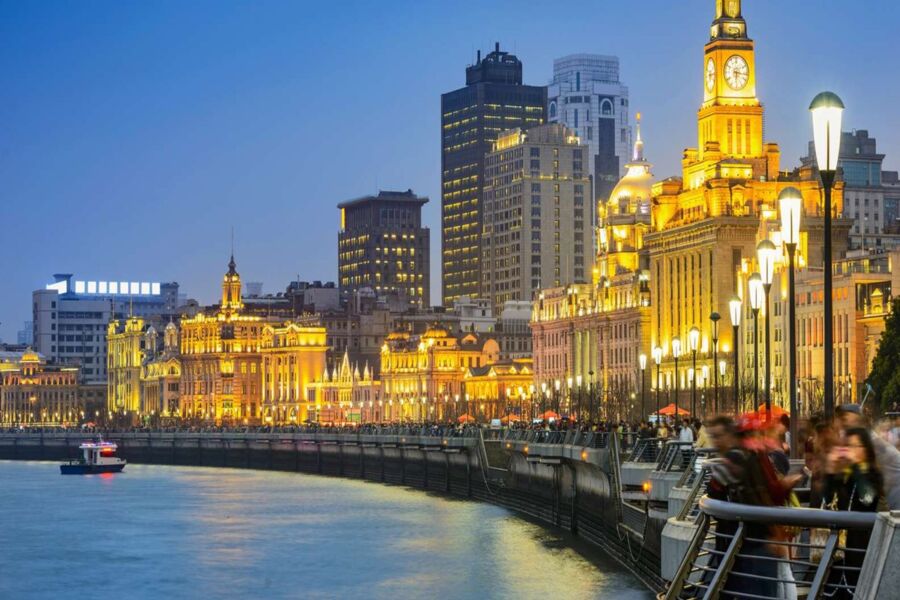 Shanghai Bund waterfront at twilight with illuminated skyline, reflecting Huangpu River, colonial, modern architecture.