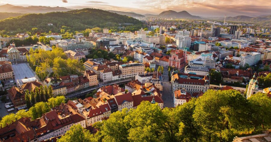 Aerial view of Ljubljana at sunset with historic and modern architecture along a river.