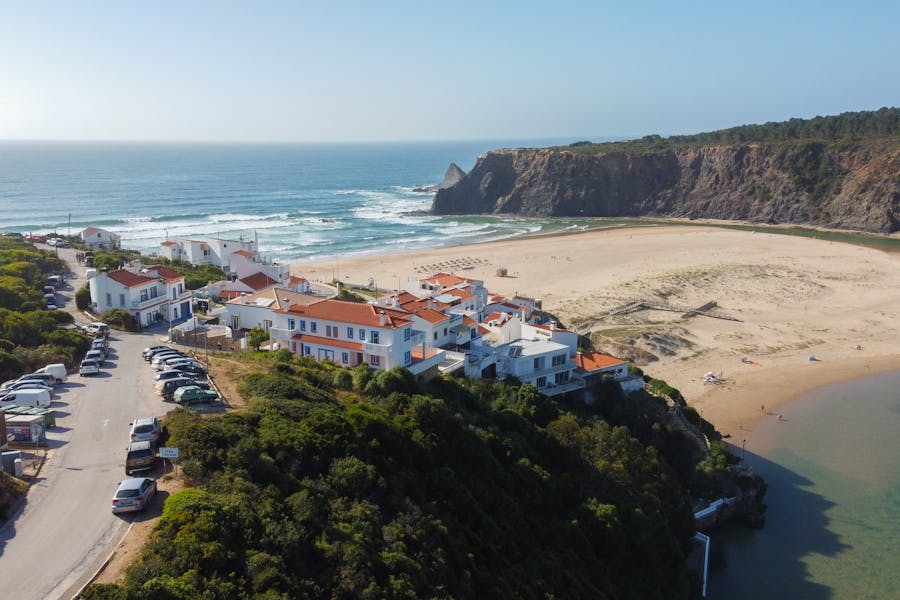 Cliffside beach village with terracotta roofs overlooking turquoise sea and wide sandy bay.