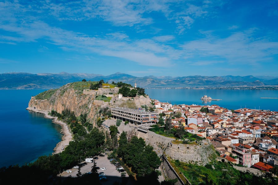 Clifftop fortress and lighthouse overlooking a Mediterranean coastal town and harbor.