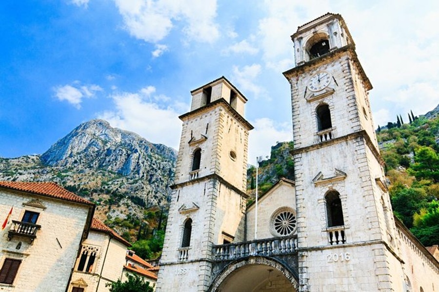 Twin towers of Cathedral of Saint Tryphon with mountain backdrop and historical architecture.