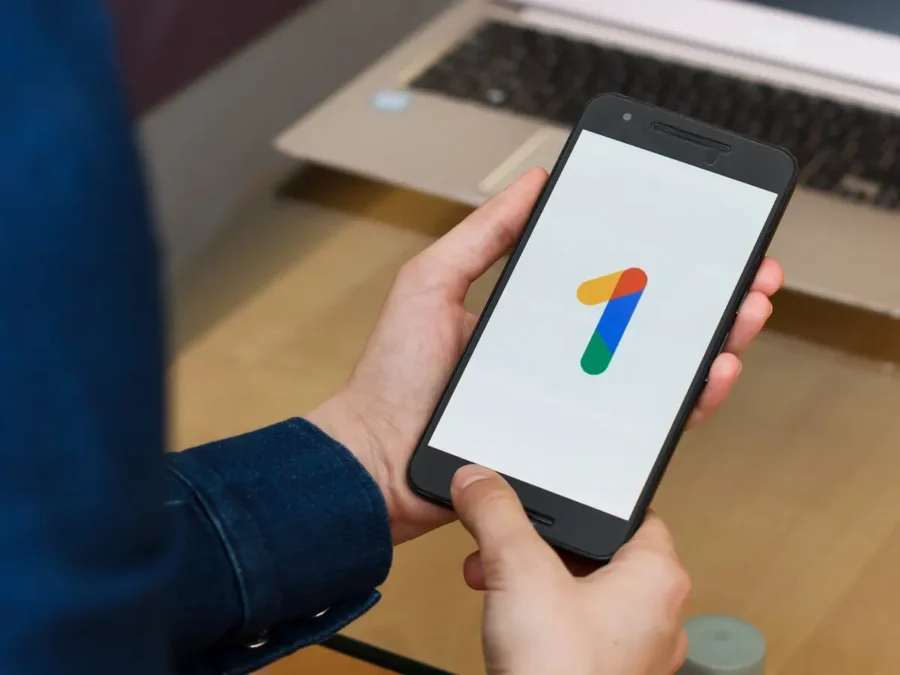 Person using Google One app on smartphone in a cozy workspace setting.