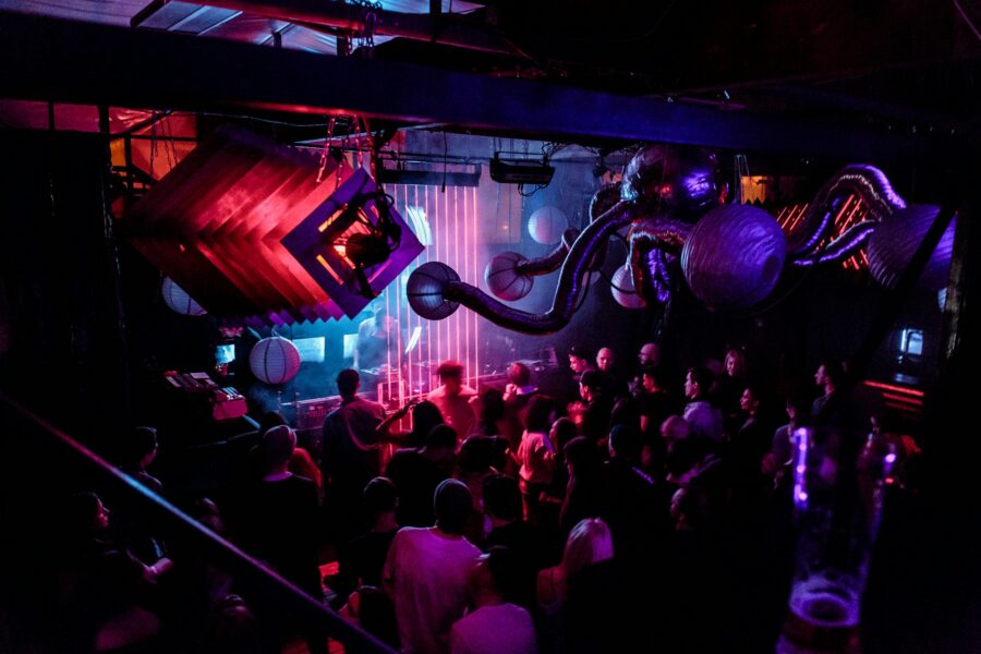 Riga nightclub crowd under neon lights and sculptural ceiling decor at live DJ stage.