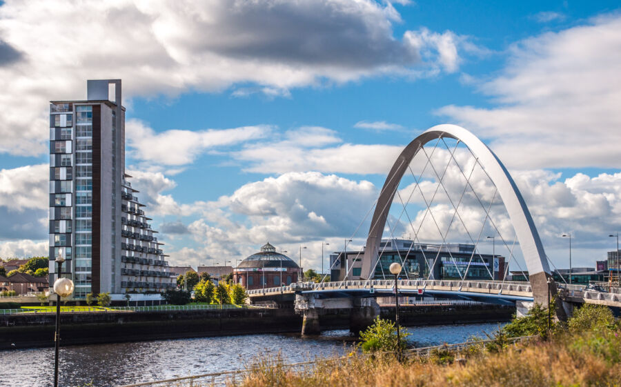 Clyde Arc bridge spans a river with a modern building visible in the background, showcasing Glasgow's urban landscape.
