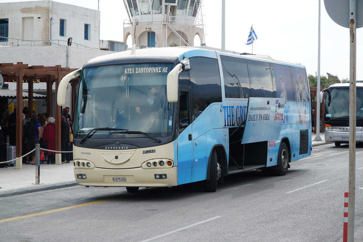 Santorini transport hub: blue-white bus KTEA Santorini AE, diverse tourists, Greek island travel.
